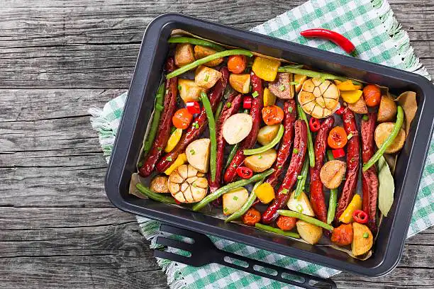 A tray filled with colorful roasted vegetables, sausages, and tomatoes arranged artistically.