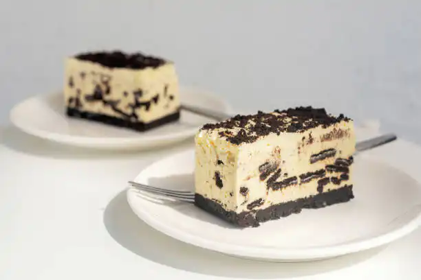 Two slices of Oreo cheesecake on white plates with forks.